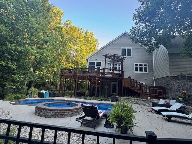Backyard with a house, deck, pool, and lounge chairs. Trees surround the outdoor space with a fence.