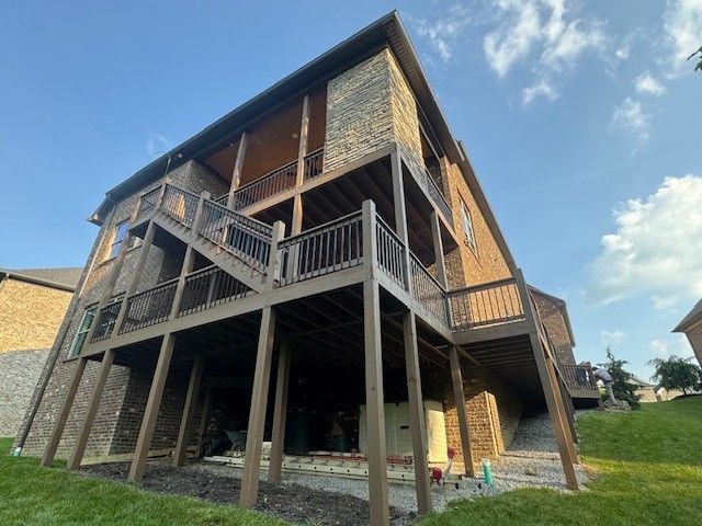 Multi-level deck on brick house, brown railings and supports. Sunny day, blue sky, grassy yard.