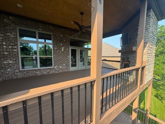 A covered deck with a brown railing, dark brown boards, and a brick wall.