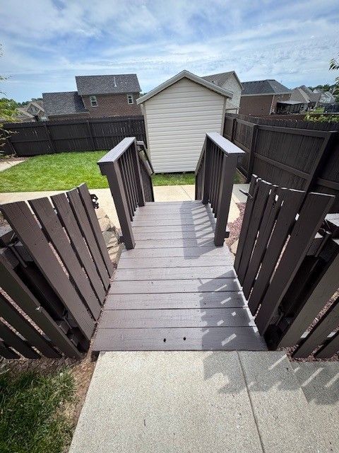 Wooden steps lead down to a backyard with a shed and brown fence under a cloudy sky.