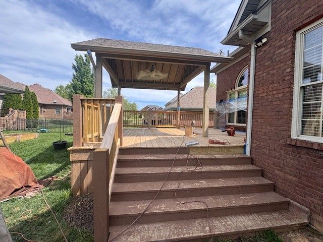 Wooden deck with steps, a gazebo, and a brick house in a backyard setting.