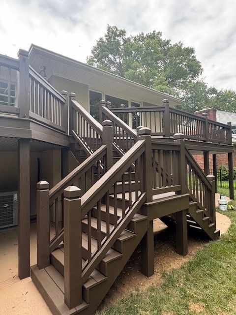 Brown two-level deck with stairs. The deck connects to a house with beige siding and a grassy lawn.