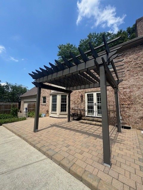 Gray pergola over a brick patio, against a brick house with a blue sky.