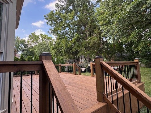 Wooden deck with black railings overlooking a grassy yard with trees under a blue sky.