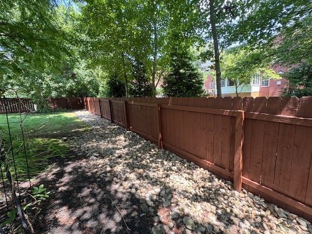 Brown wooden fence in a yard with gravel and trees, sunny setting.