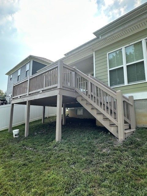 Elevated wooden deck attached to a house with stairs leading down to a grassy yard. Light brown deck with beige siding.