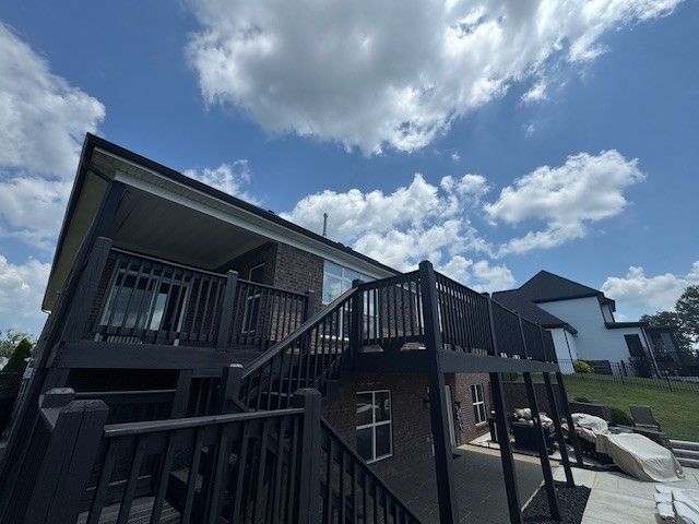 Black deck and stairs on a brick house with a blue sky and clouds.