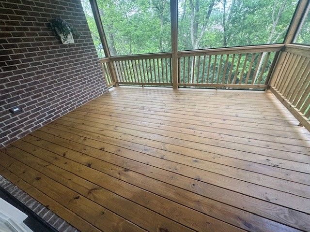 Wooden deck with brick wall and screened enclosure, overlooking a forest.