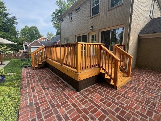 Wooden deck with railing and steps, built on a brick patio, against a beige house.