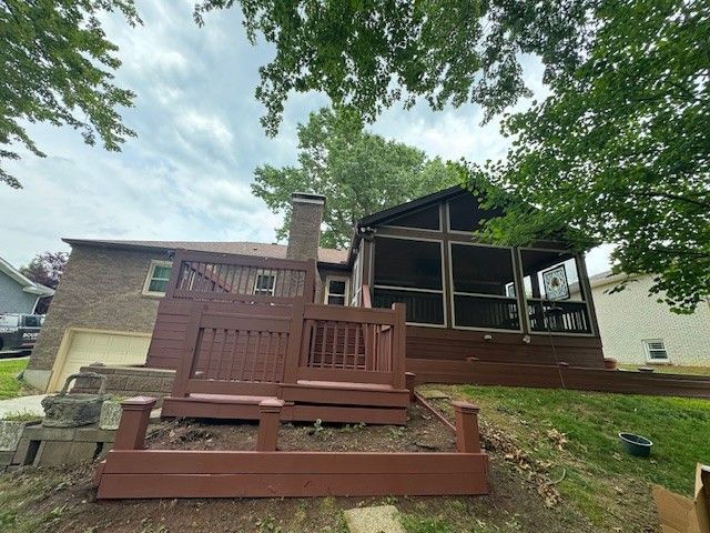Backyard with brown deck, screened porch, brick house, and green lawn under a cloudy sky.