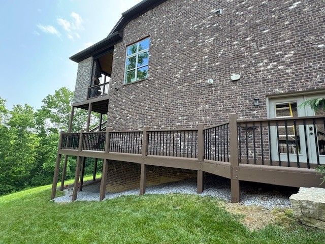 Brown brick house with a wooden deck and a sloping green lawn.