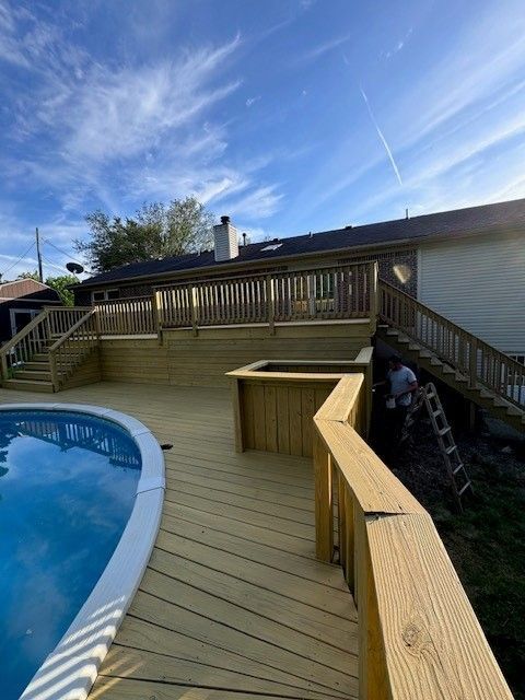 A wooden deck next to a swimming pool with a house in the background.- Bourbon City Softwash - Louisville, KY