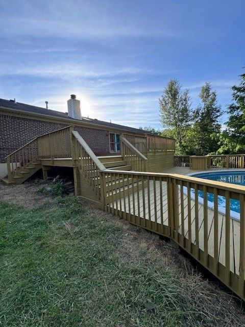 A wooden deck with stairs leading to a swimming pool in front of a house.- Bourbon City Softwash - Louisville, KY