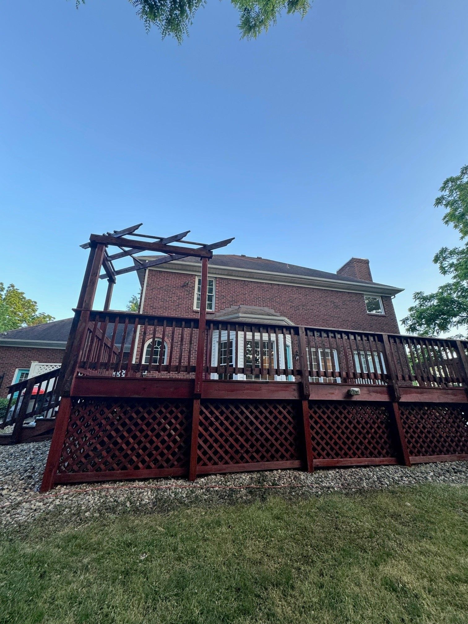 A large wooden deck with a pergola in front of a brick house. - Bourbon City Softwash - Louisville, KY