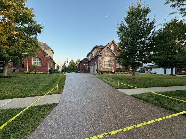 House with a brick facade and driveway cordoned off by yellow tape, trees and green lawn.