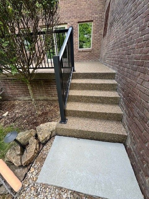 Concrete stairs with black railing leading to a door, next to a brick building.