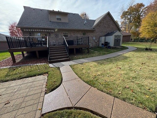 Backyard with deck, concrete path, and brick house under a cloudy sky.