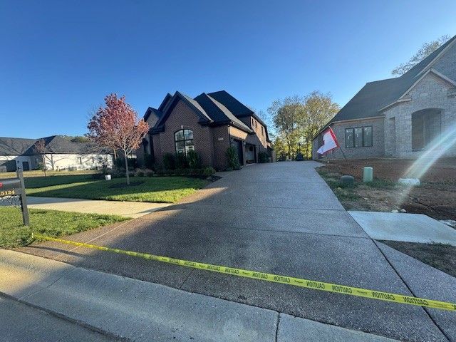 Brick house with long driveway, yellow caution tape in foreground, sunny day.