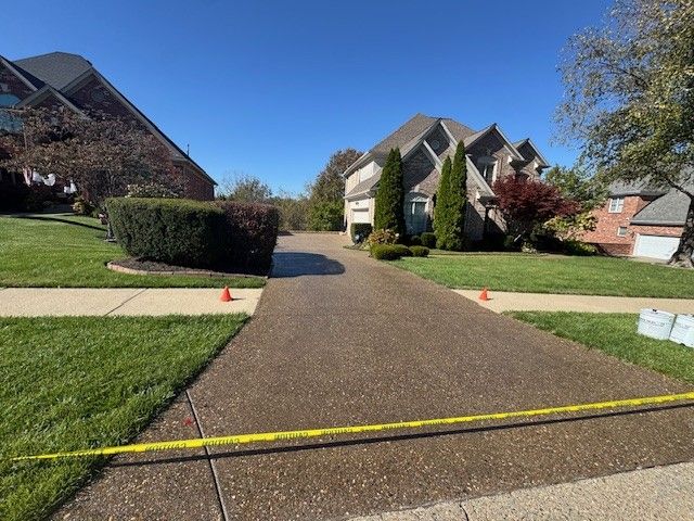 A driveway with fresh sealant, blocked off by yellow caution tape and cones, leading to a house on a sunny day.