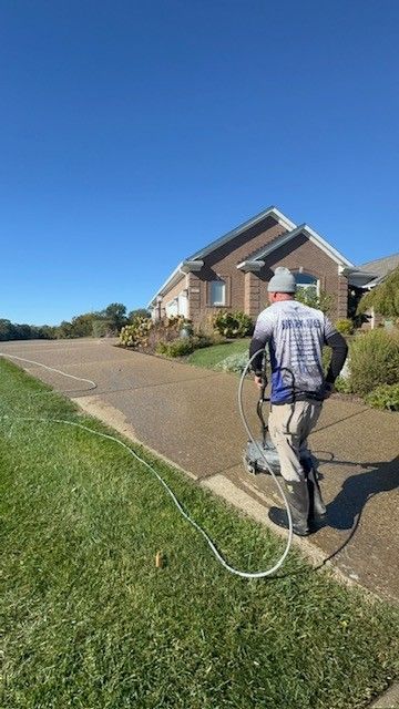 Person power washing a driveway near a house on a sunny day.
