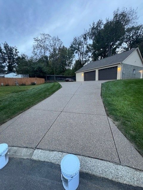 Driveway leading to a two-car garage, flanked by green grass and trees under a cloudy sky.