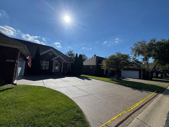 House with driveway, lawn, and sunny sky. Garage visible. Yellow caution tape on the street.