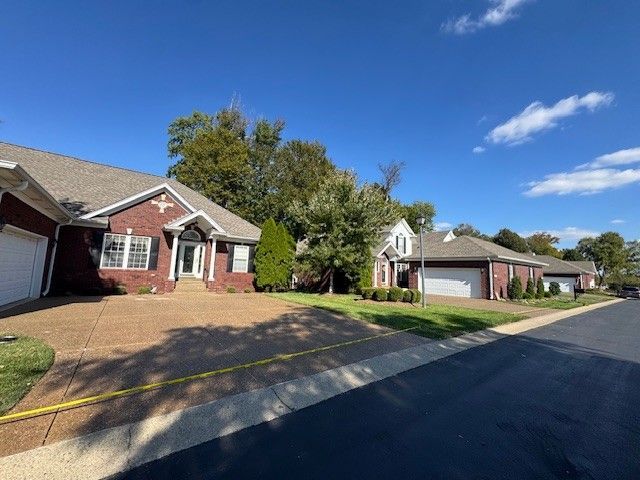 Row of brick houses with attached garages and driveways on a sunny street with blue sky.