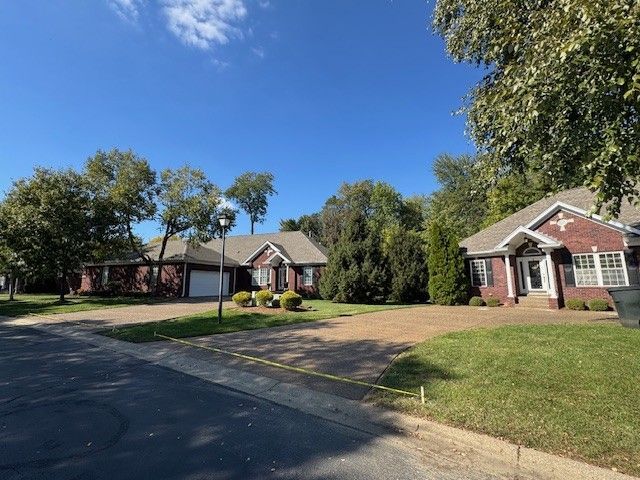 Two brick houses with driveways, trees, and a clear blue sky.
