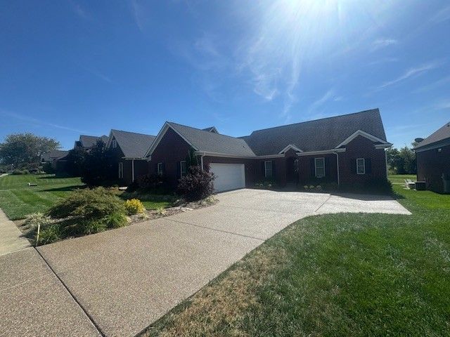 A house with a driveway and garage under a bright blue sky. Green lawn and trees surround the home.