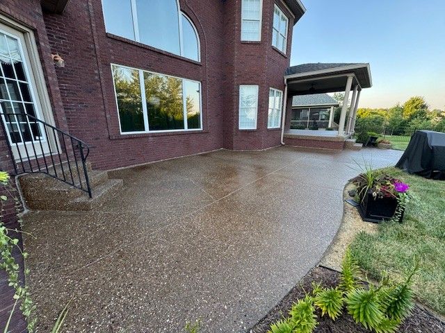 Brick house with a pebble-textured patio. A covered porch and landscaping are visible.