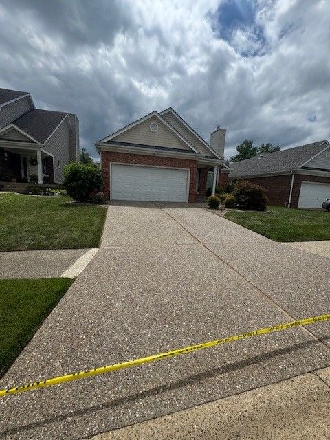 House with concrete driveway, yellow caution tape across the bottom, cloudy sky.