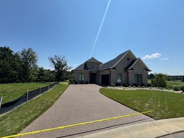 A brick house with a curved driveway, sunny day. Grass and trees surround.