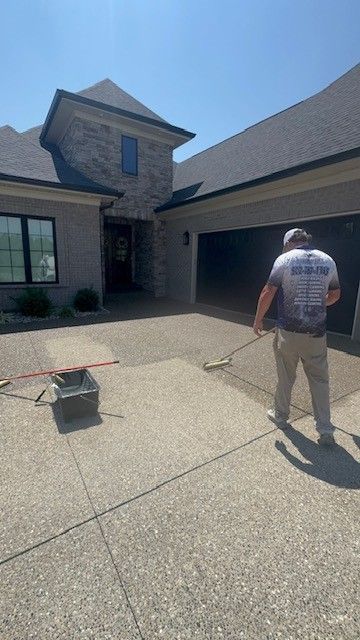A person pressure washes a concrete driveway in front of a house.