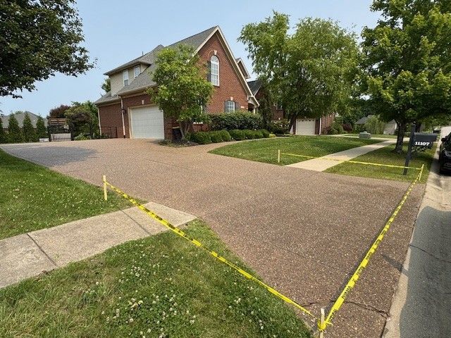 Residential driveway with yellow caution tape, next to sidewalk and green lawn, in front of a brick house.