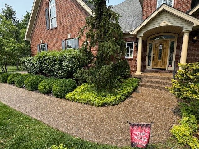Brick house with stone walkway, green bushes, and small trees in front.