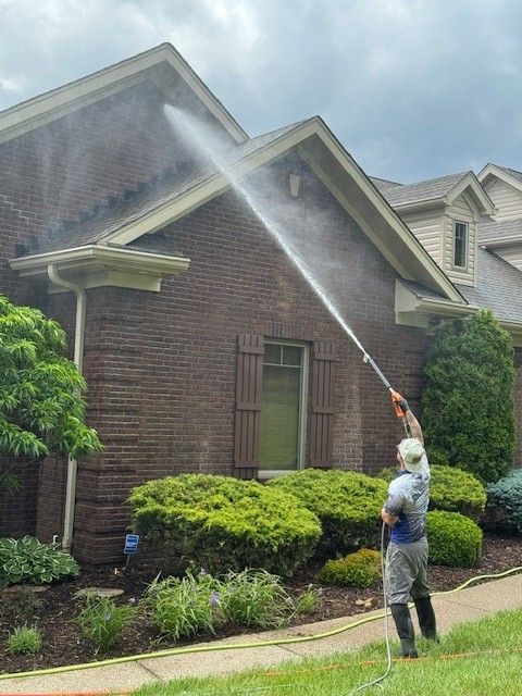 A person pressure washing the brick exterior of a house.