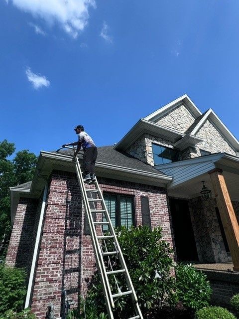 A man on a ladder is cleaning the gutters of a brick house - Bourbon City Softwash - Louisville, KY