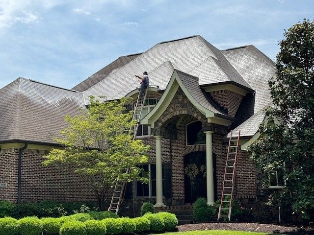 A man is painting the roof of a large brick house - Bourbon City Softwash - Louisville, KY