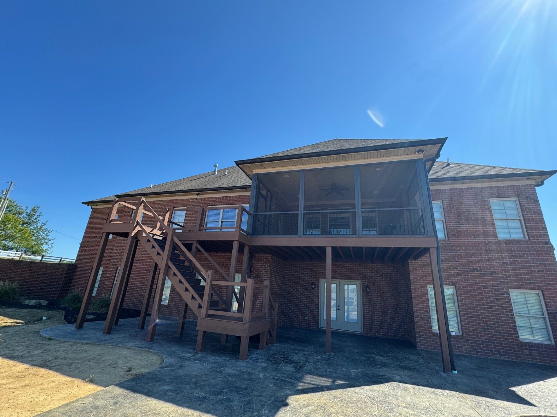 Brick house with deck, screened porch, and exterior stairs under a clear blue sky.