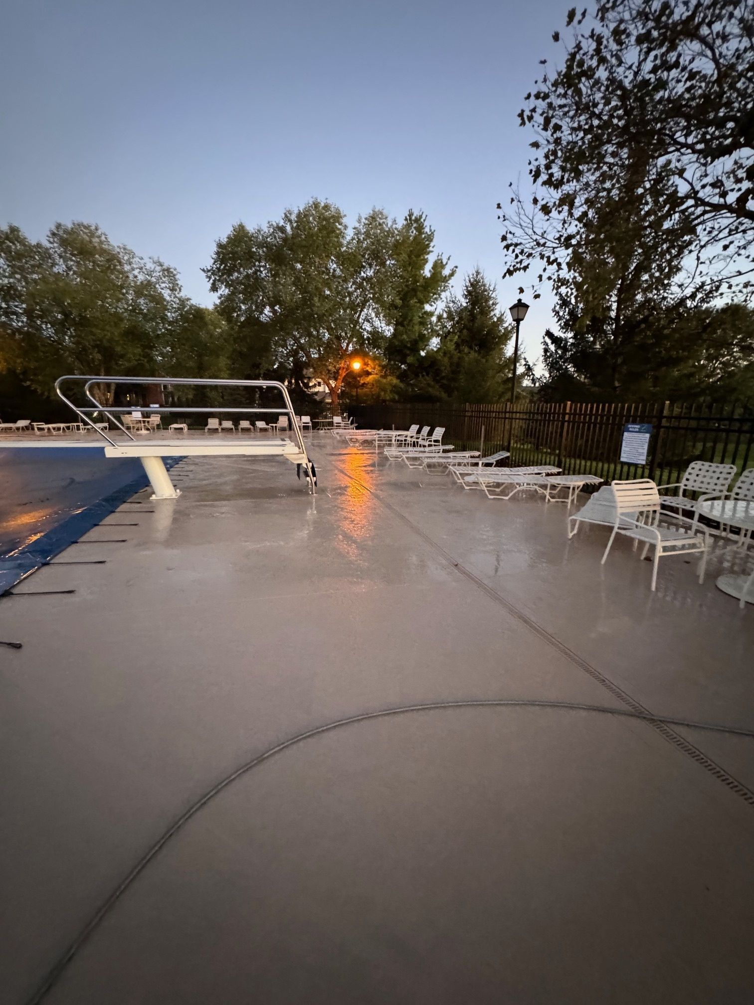A swimming pool with a diving board and chairs around it