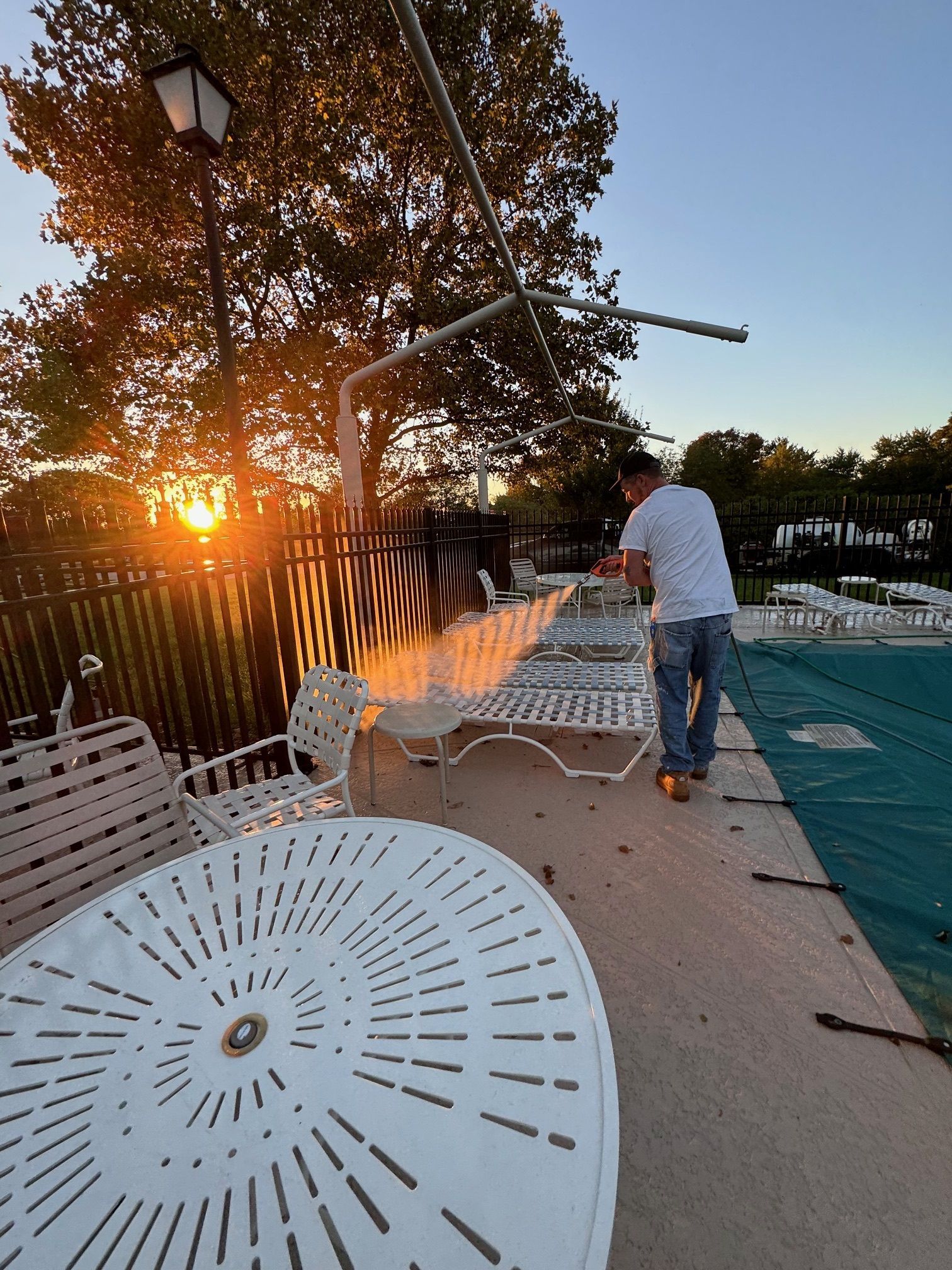 A man is standing next to a swimming pool with a table and chairs.
