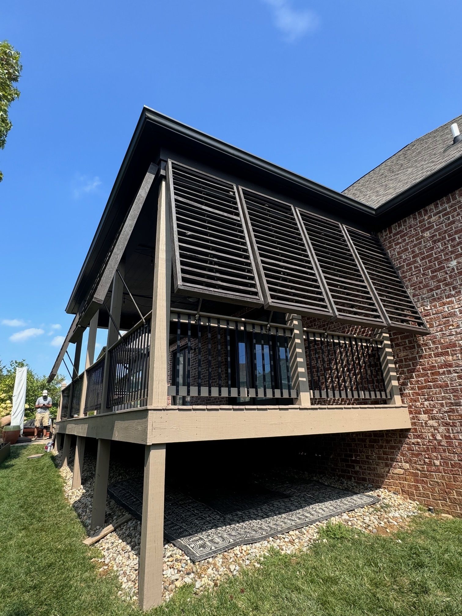 A large deck with a screened in porch next to a brick house.