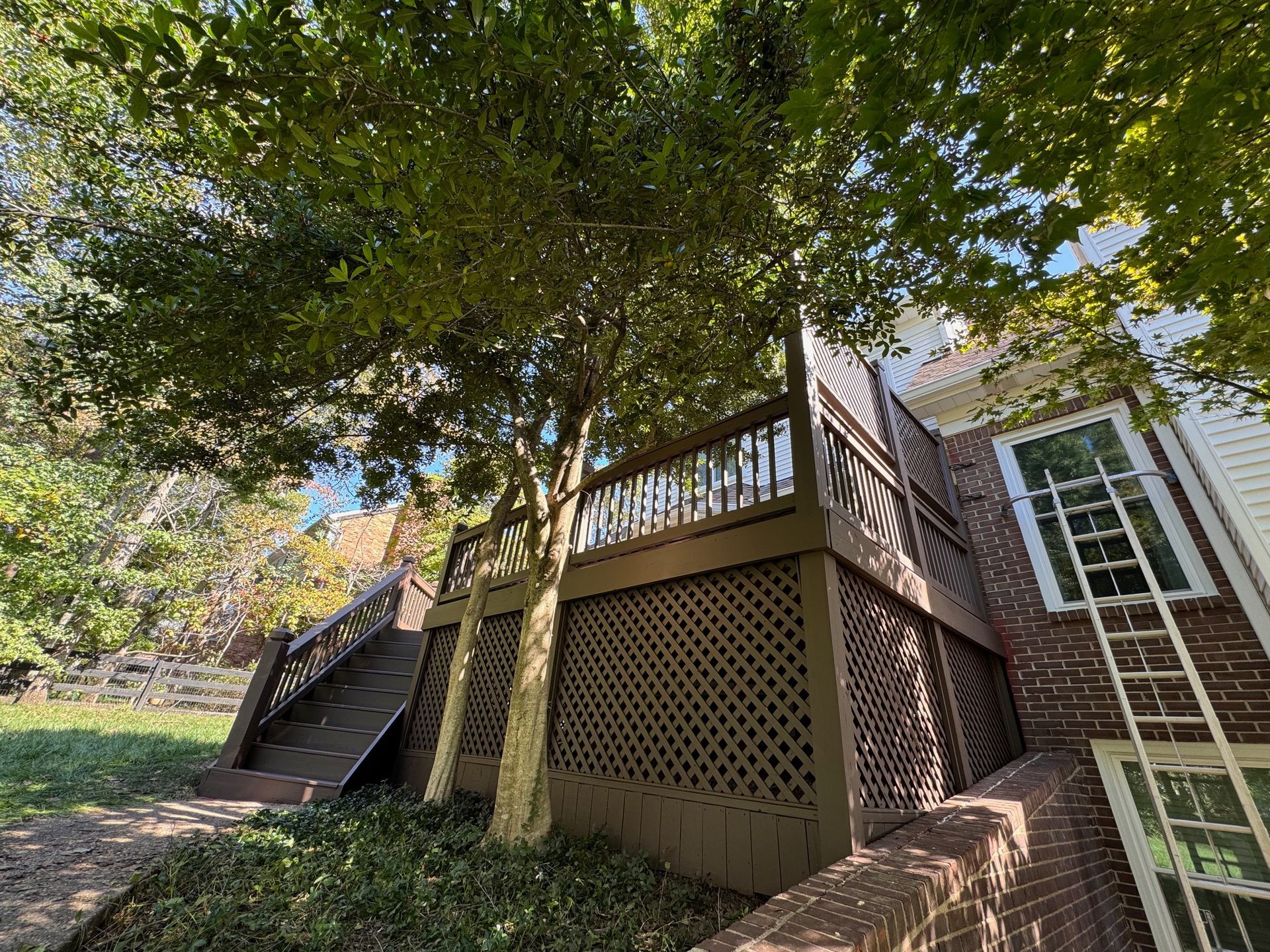 A wooden deck with stairs leading up to it is in front of a brick house.