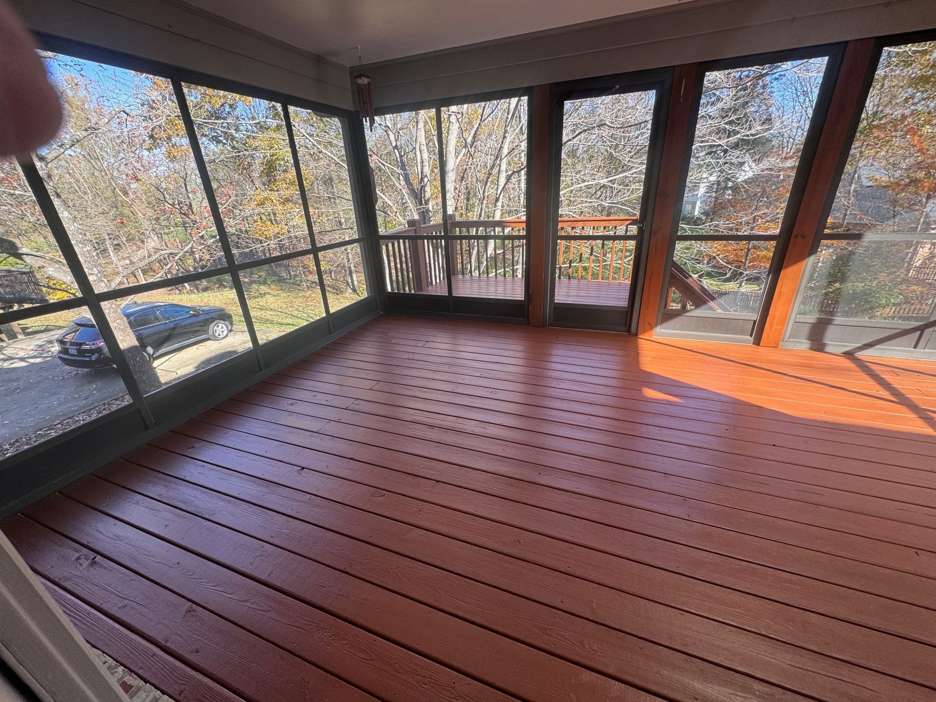A screened in porch with a wooden deck and lots of windows.