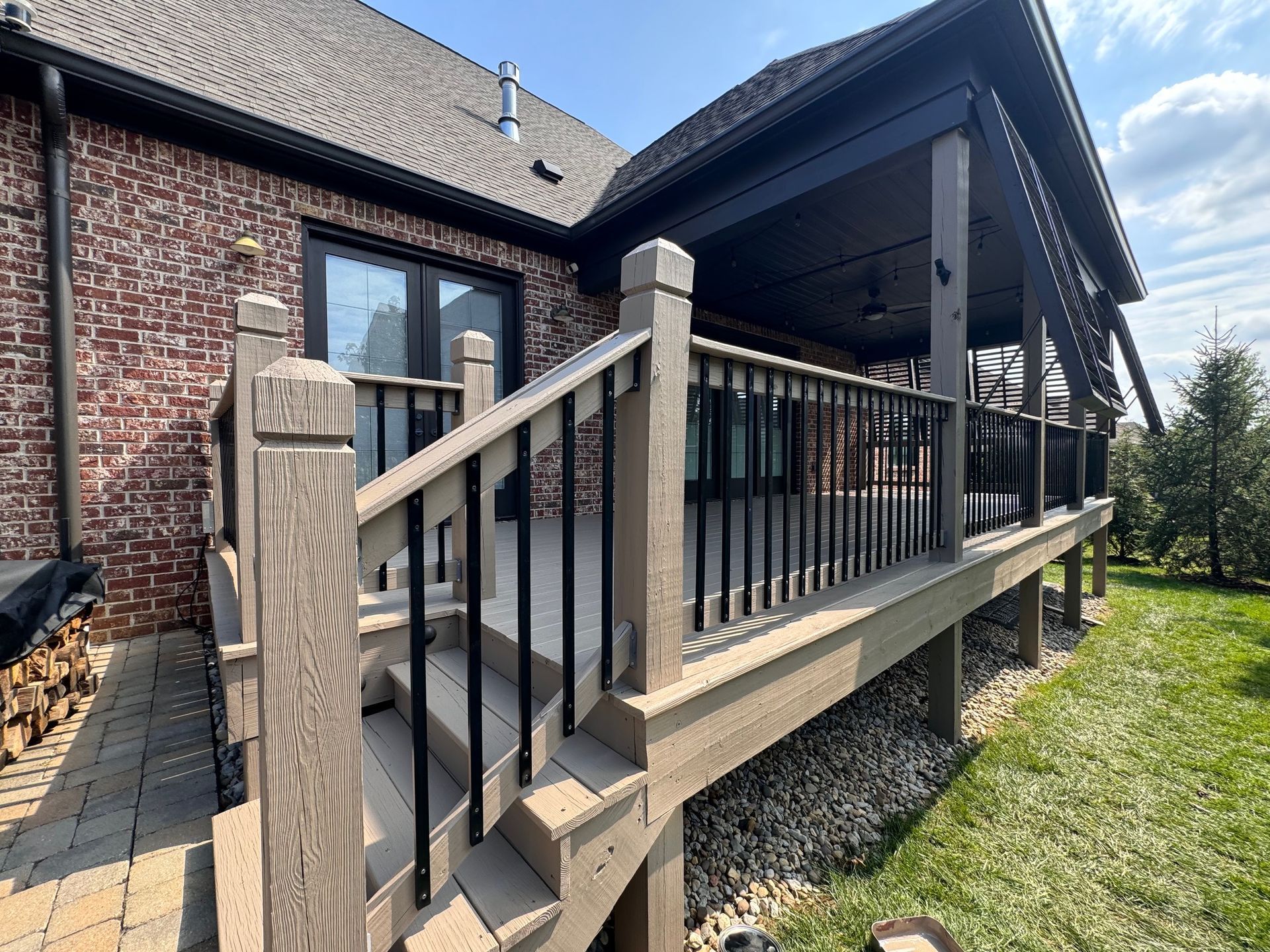 A large deck with stairs leading up to it is in front of a brick house.
