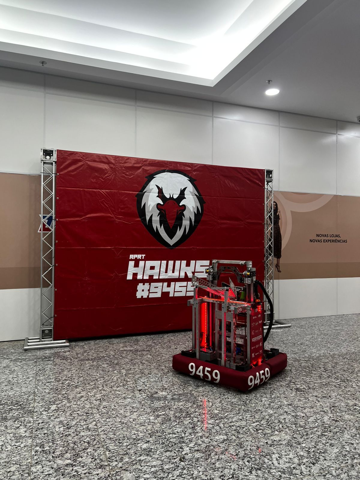 A robot stands in front of a red banner with the team's logo and name.