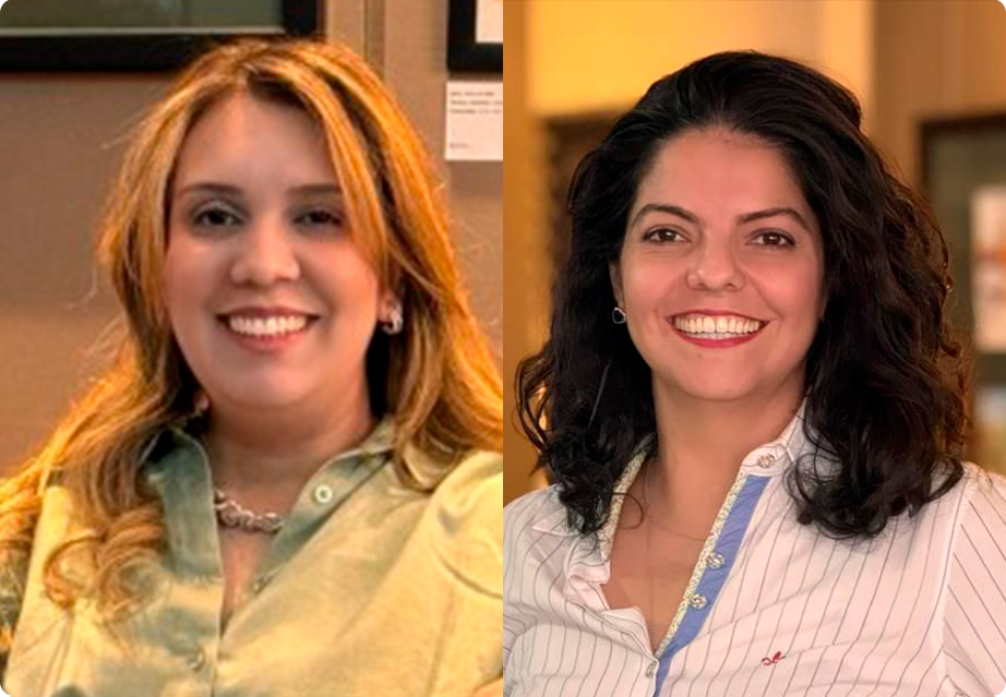 Duas mulheres sorridentes em pé dentro de um ambiente fechado, uma vestindo uma camisa verde e a outra uma camisa listrada branca.