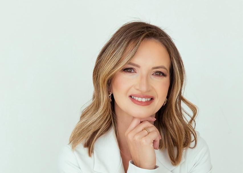 Uma mulher de jaleco branco está sorrindo com a mão no queixo.