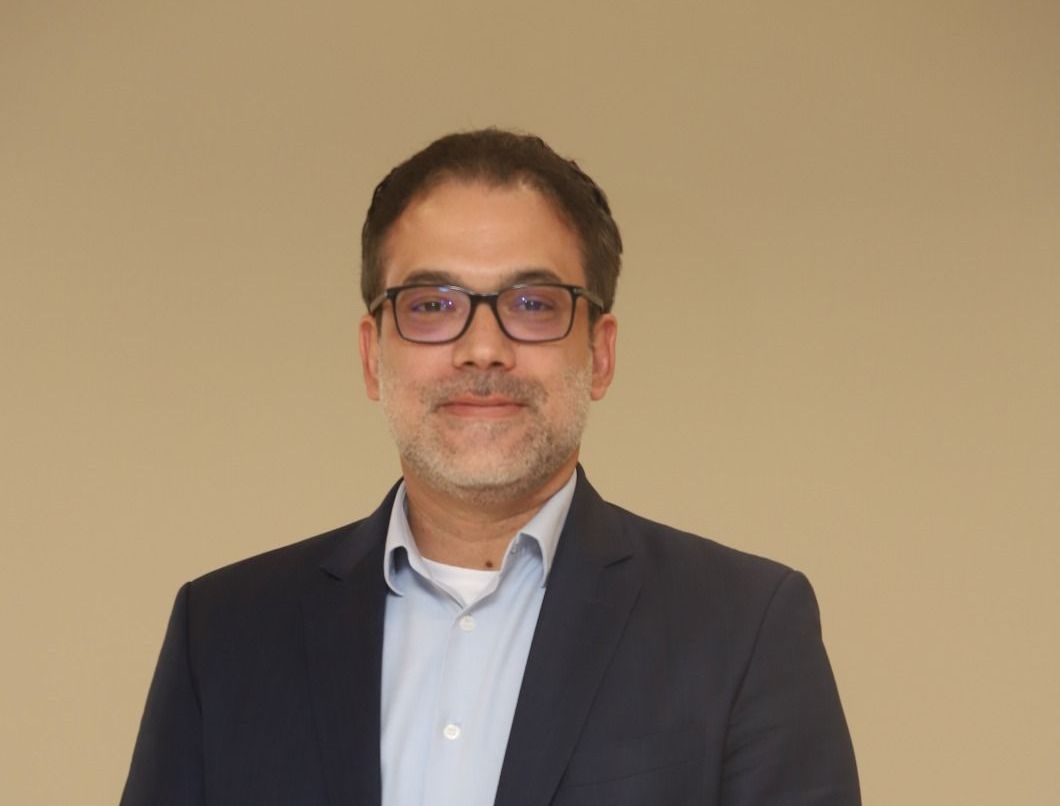 A man in a suit and glasses is standing with his hands on his hips.