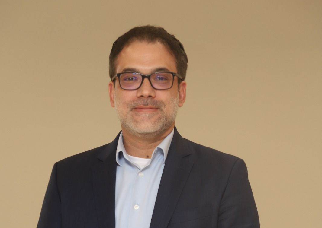 Um homem de terno e óculos está sorrindo para a câmera.